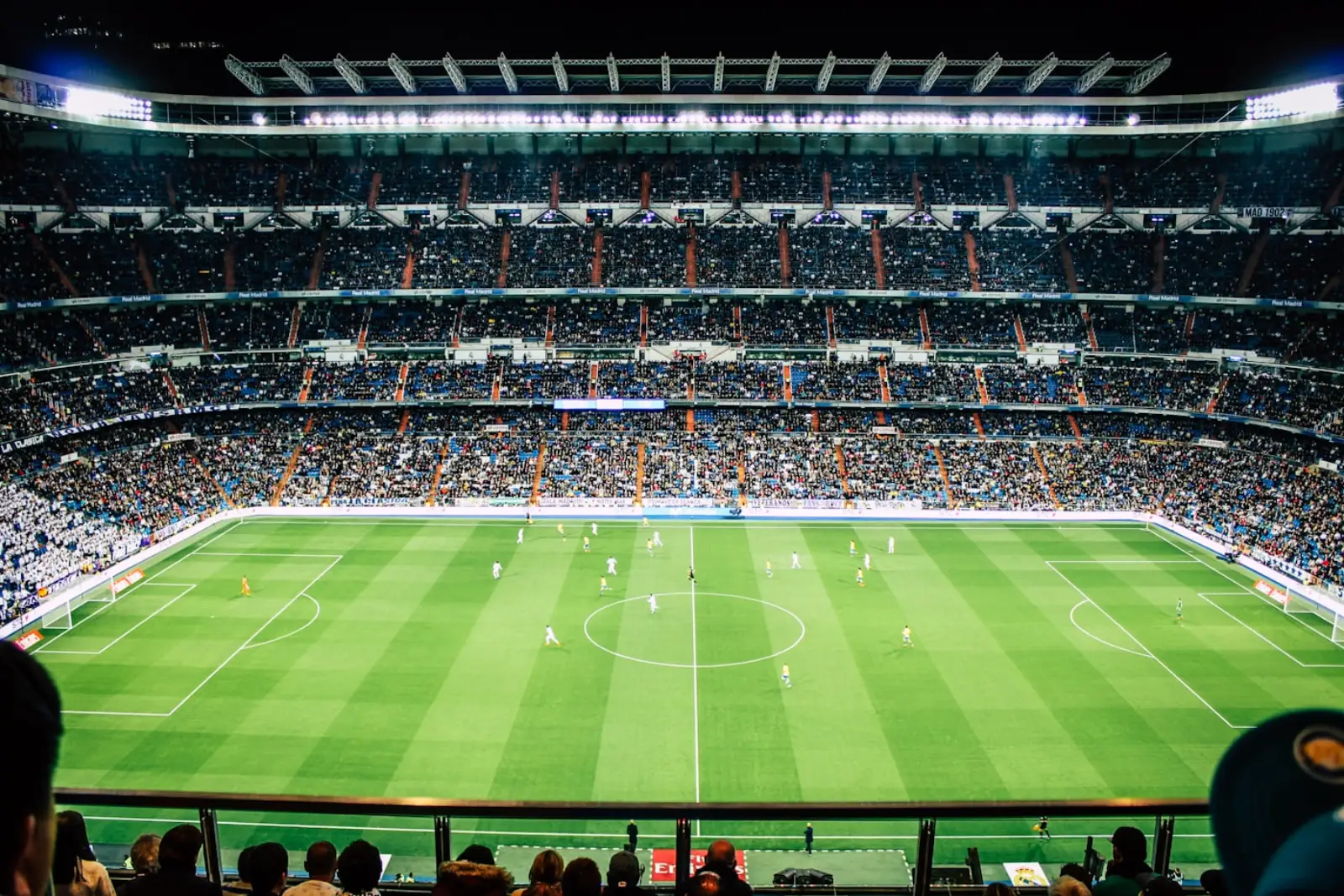 Estádio de futebol cheio, à noite, sob os holofotes durante um jogo
