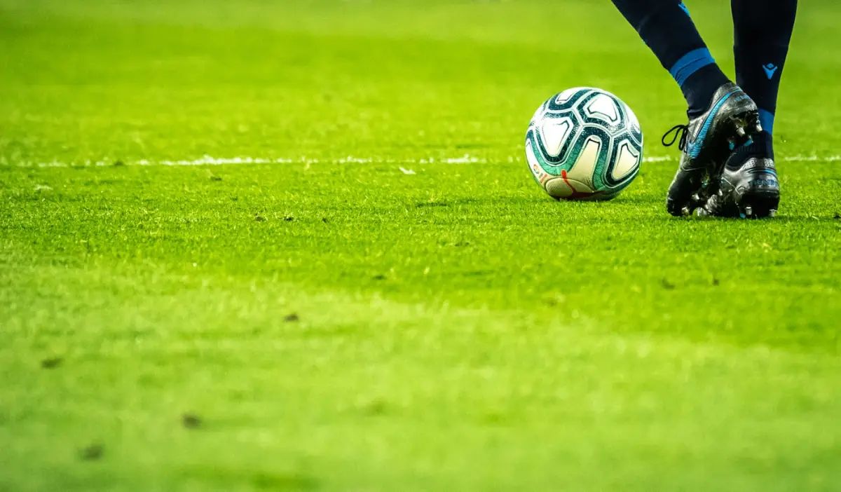 Bola de futebol e chuteira na relva, junto à linha de campo